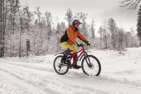 Mann fährt Mountainbike auf einem Weg im Winterwald, lizenzfreies Stockfoto