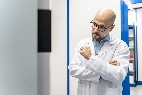 Mann mit Laborkittel und Brille schaut auf eine Maschine, lizenzfreies Stockfoto