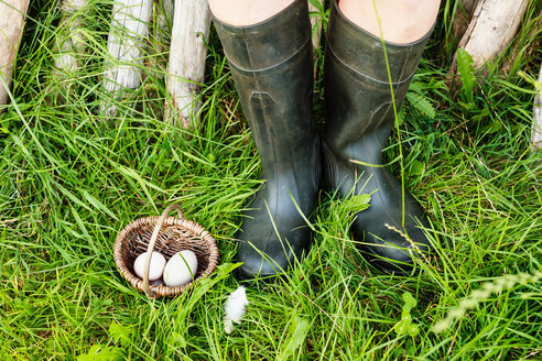 Two eggs in basket beside pair of legs wearing boots - CUF49897