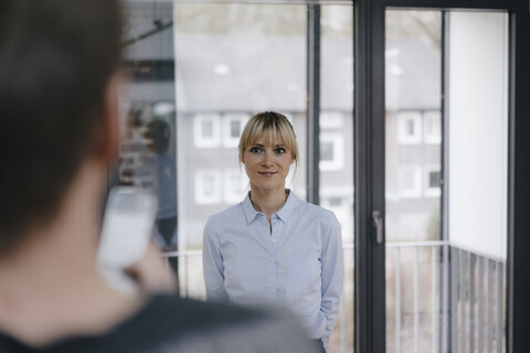 Blonde Geschäftsfrau steht im Büro und sieht einen Kollegen an, lizenzfreies Stockfoto