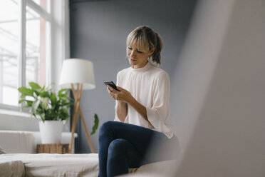 Frau sitzt auf der Couch und benutzt ihr Smartphone - JOSF03139