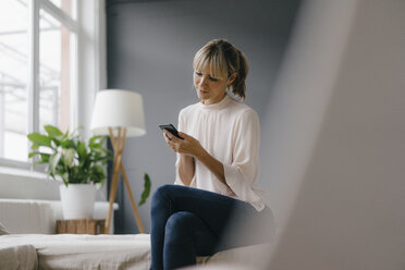 Woman sitting on couch, using smartphone - JOSF03139