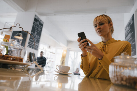 Blonde Geschäftsfrau, die in einem Café ihr Smartphone benutzt und Textnachrichten liest, lizenzfreies Stockfoto