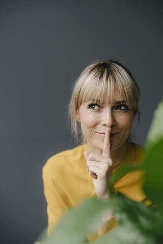 Porträt einer schönen blonden Frau, die lächelt und den Finger auf den Mund legt, lizenzfreies Stockfoto