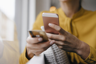 Blonde Geschäftsfrau sitzt am Fenster und bezahlt mit Smartphone und Kreditkarte - JOSF03148