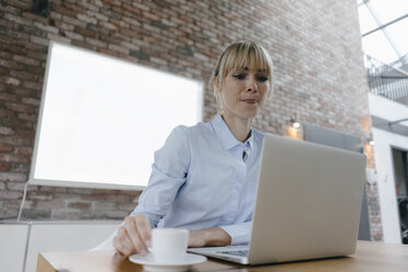 Businesswoman working on laptop, drinking coffee, licking lips - JOSF03150