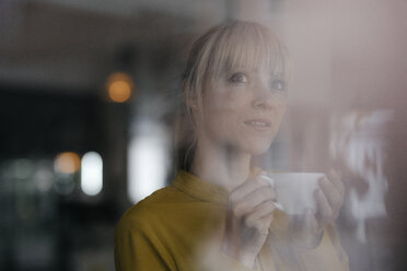 Portrait of a beautiful blond woman standing at window, drinking coffee - JOSF03162