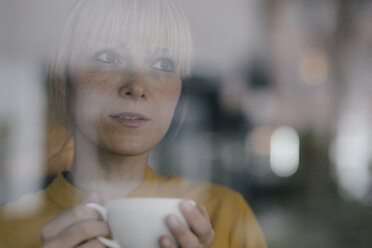 Porträt einer schönen blonden Frau, die am Fenster steht und Kaffee trinkt - JOSF03167