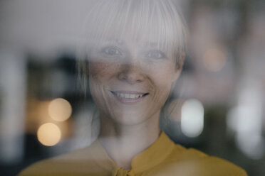 Portrait of a beautiful blond woman standing at window, smiling - JOSF03168