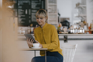 Blond businesswoman using smartphone in a coffee shop, reading text messages - JOSF03170