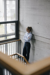 Successful businesswoman leaning on wall, looking out of window, with arms crossed - JOSF03177