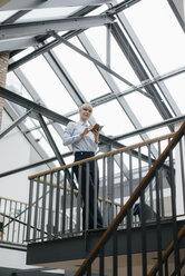 Businesswoman standing in loft office, using smartphone - JOSF03183