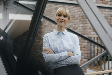 Confident woman sitting in offeice building with arms crossed - JOSF03187