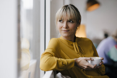 Porträt einer schönen blonden Frau, die am Fenster sitzt und Kaffee trinkt - JOSF03188