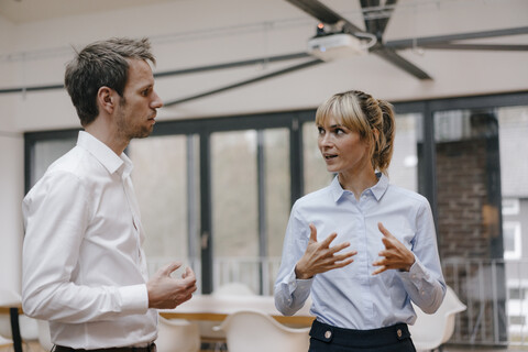 Geschäftsmann und Frau stehen in einem Büro und unterhalten sich, lizenzfreies Stockfoto