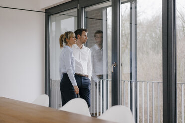 Successful businesswoman and businessman in conference room, looking out of window - JOSF03221