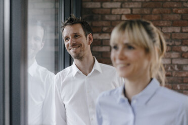 Successful businesswoman and businessman looking out of window, smiling - JOSF03224