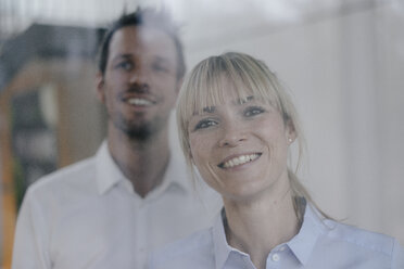 Successful businesswoman and businessman looking out of window, smiling - JOSF03227