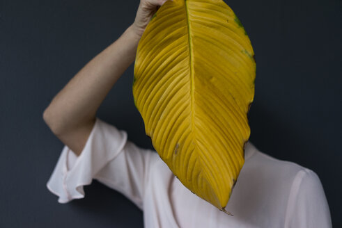 Frau bedeckt ihr Gesicht mit einem gelben Bananenblatt - JOSF03274