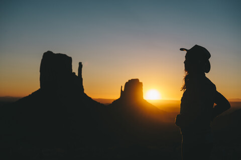 USA, Utah, Monument Valley, Silhouette einer Frau mit Cowboyhut bei Sonnenaufgang, lizenzfreies Stockfoto