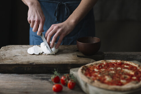 Young man preparing pizza, cutting mozzarella on chopping board - ALBF00805