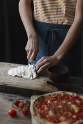 Young man preparing pizza, cutting mozzarella on chopping board - ALBF00806