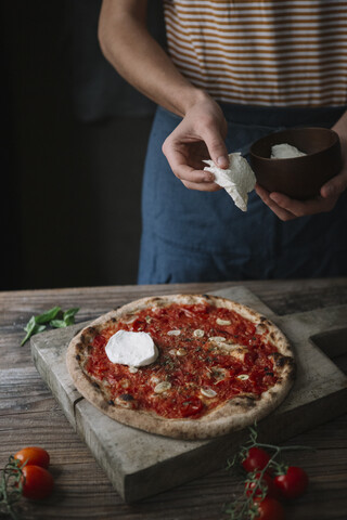 Junger Mann bereitet Pizza zu, hält Mozzarella in der Hand, lizenzfreies Stockfoto