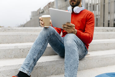 Casual businessman sitting stairs in the city, using his digital tablet and headphones - JRFF02833