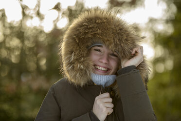 Portrait of laughing young woman wearing hood with fur trimming in winter - LBF02432