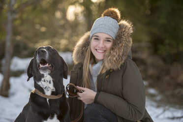 Porträt einer glücklichen jungen Frau mit Hund im Winterwald - LBF02433