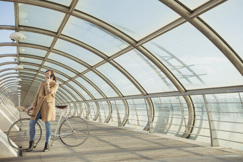 Junge Hipster-Frau mit einem Fahrrad in einem modernen Tunnel, die telefoniert - AHSF00043