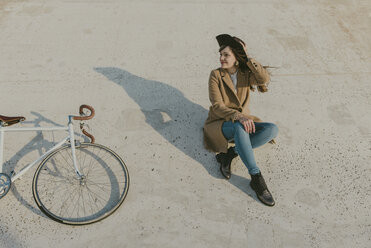Junge Hipster-Frau sitzt neben einem Fahrrad - AHSF00045