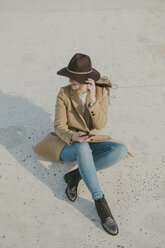 Young hipster woman sitting on the ground holding a phone - AHSF00046
