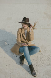 Young hipster woman sitting on the ground holding a phone - AHSF00047