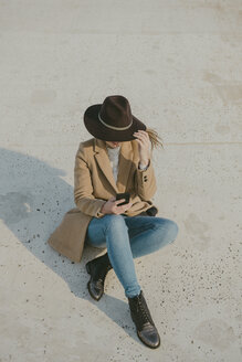 Young hipster woman sitting on the ground holding a phone - AHSF00049