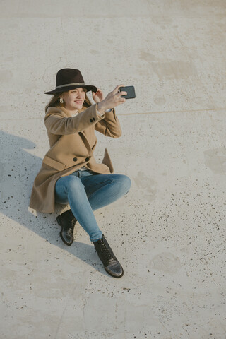 junge Hipster-Frau sitzt auf dem Boden und macht ein Selfie, lizenzfreies Stockfoto