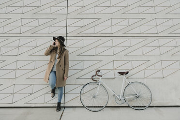 Junge Hipster-Frau, die in der Nähe eines Fahrrads telefoniert - AHSF00053