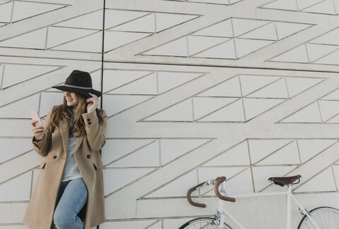 Junge Hipster-Frau in der Nähe eines Fahrrads hält ein Telefon, lizenzfreies Stockfoto