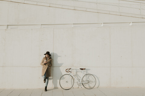Junge Hipster-Frau lehnt neben einem Fahrrad und hält ein Telefon, lizenzfreies Stockfoto