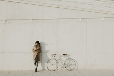Junge Hipster-Frau lehnt neben einem Fahrrad und hält ein Telefon - AHSF00060