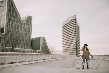 Junge Hipster-Frau mit einem Fahrrad auf einer Brücke in der Stadt - AHSF00069