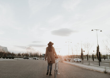 Young hipster woman going with a bicycle during sunset - AHSF00070