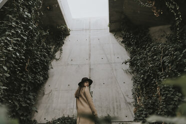 Young woman in underground tunnel, concrete wall full of plants - AHSF00074