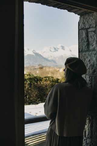 Rückansicht einer Frau, die in die Ferne schaut und sich ins Fenster lehnt, lizenzfreies Stockfoto