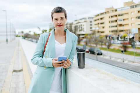Woman dressed in jacket suit with smartphone and thermo mug stock photo