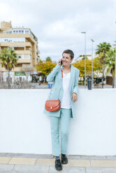 Woman dressed in jacket suit using smartphone, with thermo mug - KIJF02422