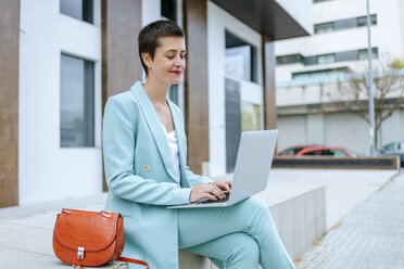 Woman in suit jacket using laptop outdoors - KIJF02427