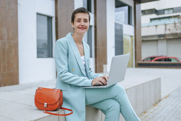 Woman in suit jacket using laptop outdoors - KIJF02428