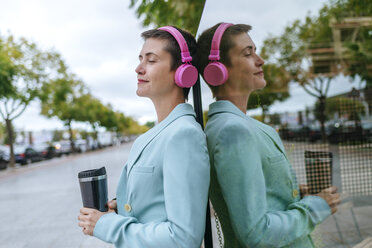 Woman dressed in jacket with thermo mug and pink headphones, reflection - KIJF02434