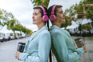 Woman dressed in jacket with thermo mug and pink headphones, reflection - KIJF02435